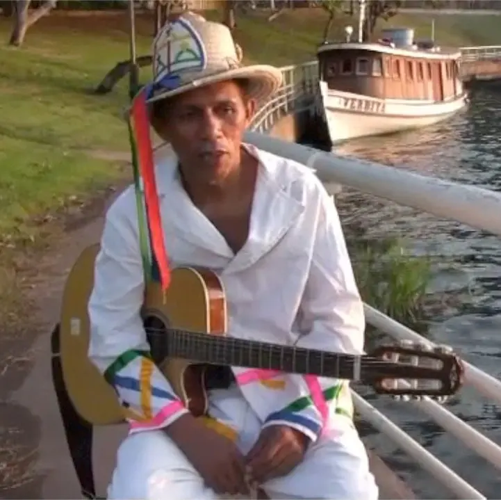 Chico Malta com violão e chapéu de fita
